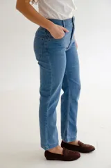 Jean de corte recto y tiro medio, confeccionado en denim azul clásico. Presenta diseño de cinco bolsillos con costuras reforzadas y cierre frontal con botón metálico.