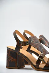 Sandalia de taco medio cuadrado, confeccionada en cuero con textura de piel de serpiente. Presenta un diseño de tiras cruzadas con hebillas metálicas ajustables y cierre de pulsera al tobillo.