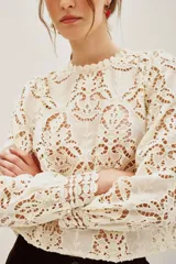 Camisa de encaje negro con cuello alto y mangas largas abullonadas. Presenta un diseño calado con motivos florales y cierre posterior.