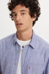 Camisa de manga corta Levi's en color azul con textura tipo chambray. Presenta cuello clásico, cierre frontal con botones y un bolsillo en el pecho con la etiqueta roja característica de la marca.