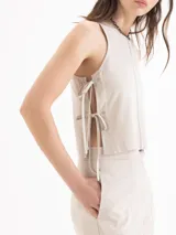 Top de twill color beige, de silueta recta y diseño sin mangas con cuello redondo. Se destaca por sus aberturas laterales con lazos regulables y remaches metálicos.