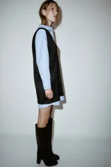 Vestido corto que combina una camisa celeste de manga larga con cuello solapa y botones frontales, con un chaleco de tejido negro sin mangas y escote en V superpuesto.