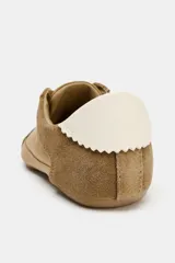 Zapatilla estilo blucher de diseño deportivo, confeccionada en una combinación de materiales lisos y gamuzados en tonos tostados, con detalle de talón en color blanco y cierre mediante cordones.