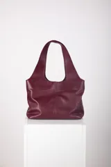 Bolso tote de cuero marrón oscuro, de gran tamaño y diseño minimalista, con asas integradas y costuras verticales visibles en el frente.