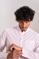 Camisa de manga larga confeccionada en tejido poplin con diseño de rayas verticales finas en color rosado y blanco. Presenta cuello abotonado (button-down), cierre frontal con botones y un bolsillo en el pecho.