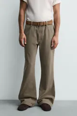 Pantalón de denim color verde oliva, estilo chino con corte ancho y bota acampanada (flare) desde la rodilla. Tiro medio, confeccionado en tejido rígido. Presenta bolsillos frontales y bolsillos traseros de plastrón.