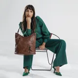Cartera estilo hobo color marrón, confeccionada en material símil cuero con textura. Presenta dos bolsillos frontales con cierre metálico, apertura superior con cierre y asa corta para el hombro.