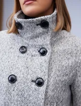 Tapado corto de lana y poliéster, con tejido tweed en tonos blanco y negro. Presenta cuello con solapa, doble abotonadura frontal en color negro y bolsillos verticales.