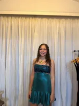 Vestido corto negro con diseño cut-out en la cintura y detalle de encaje en el centro del busto. Presenta breteles finos, falda con volado en el ruedo y flecos decorativos.