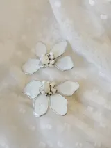 Par de aros colgantes con forma de flor blanca con borde plateado y centro de perlas y cuentas plateadas.