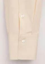 Blusa oversize de algodón en color marfil, con cuello camisero alto, manga larga con puños abotonados y cierre frontal de botonadura oculta.