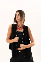 Chaleco oversize de cuero descarne color negro, con diseño de terminación en picos, flecos en la espalda y detalle de tachas metálicas a lo largo de los bordes frontales.