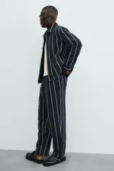 Sobrecamisa de hombre, corte relajado, color azul marino con rayas verticales blancas. Presenta cuello solapa, manga larga con puños abotonados, bolsillos de parche delanteros y cierre frontal de botones.