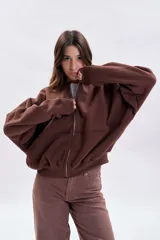 Campera oversize color marrón con cierre frontal, mangas amplias y diseño con cortes horizontales. Presenta puños y ruedo acanalados.