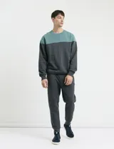 Sweater de tejido circular con diseño color block, combinando una franja superior en color verde y el resto de la prenda en gris oscuro. Presenta cuello redondo y puños en tejido canalé.