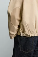 Cazadora relaxed fit de Zara confeccionada en denim de algodón color beige, con cuello de solapa en piel combinada, bolsillos con cremallera en el pecho y cierre frontal oculto.