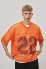 Remera de malla color naranja vibrante, estilo jersey de fútbol americano, con cuello en V y corte oversized. Presenta un estampado grande y desgastado del número "22" en color negro o marrón oscuro en el frente.