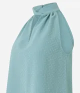 Blusa sin mangas color verde menta, confeccionada en tejido jacquard con textura de pequeños cuadros. Presenta un cuello halter que se anuda o cruza en la parte delantera, creando un escote en V con un recorte central.