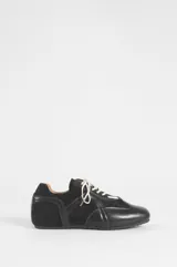 Zapatillas negras de estilo urbano con cordones blancos, confeccionadas en cuero sintético y poliéster, con diseño de paneles y suela plana.