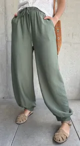 Pantalón tipo babucha de color verde militar, con cintura elástica fruncida y cordón ajustable. Cuenta con diseño amplio y puños elásticos en los tobillos.