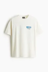 Remera de algodón color crema con cuello redondo acanalado y mangas cortas. Presenta un estampado pequeño en el pecho con el logo de Nirvana y la leyenda Unplugged in New York.