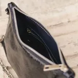 Cartera tipo media luna de cuero natural color marrón, con cierre superior y correa de cadena metálica plateada. Presenta el logo de la marca grabado en el frente.