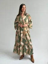 Vestido largo verde con estampado botánico en tonos tostados, escote en V con botones frontales, mangas largas abullonadas y diseño en niveles con volados.