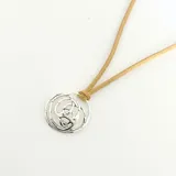 Collar con dije circular de plata 950 con diseño abstracto y cordón de cuero color beige.