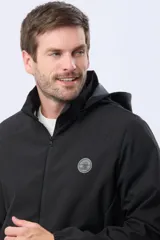 Campera repelente al agua y cortaviento de color negro, con capucha desmontable, cierre frontal y parche circular en el pecho.