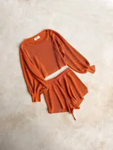 Buzo de tejido de punto con acabado brillante, confeccionado con hilado italiano. Presenta cuello redondo, mangas largas acampanadas y un corte holgado.