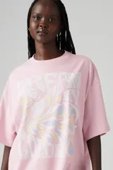 Remera rosa de corte holgado con estampado de texto e imagen abstracta en el frente.