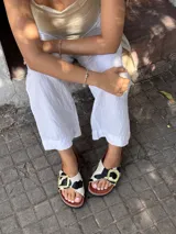 Sandalias bajas con base de corcho y tira ancha de pelo con estampado de vaca y hebilla dorada.