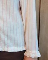 Camisa de manga larga con estampado de rayas verticales en tonos crudo y beige. Presenta cuello alto con volados, cierre frontal con botones dobles y puños con volados.