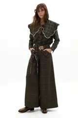 Camisa de manga larga confeccionada en popelina de algodón con estampado de cuadros en tonos verde oscuro y amarillo. Presenta un cuello amplio con bordes ondulados y terminaciones en encaje de algodón crudo, cierre frontal con botones de nácar y lazo de ajuste en el cuello.