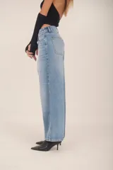 Pantalón de jean color beige claro, tiro medio, con corte ancho y pierna recta. Presenta costuras visibles en tono contrastante.