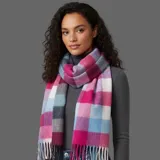 Bufanda rectangular de tejido grueso con diseño de cuadros en tonos fucsia, rosa, celeste, blanco y gris. Presenta flecos en los extremos.