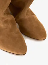 Bota de gamuza color marrón claro con caña media, punta fina y taco geométrico de madera color negro. El borde superior de la bota está doblado hacia afuera.