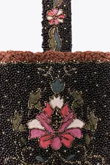 Bolso pequeño de mano con asa corta, confeccionado con abalorios negros y diseño floral bordado en tonos rosa y verde. Presenta flecos largos de abalorios en la parte inferior y cierre con botón a presión.
