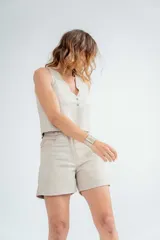 Short de cuero color beige, tiro alto, con bolsillos laterales y cierre frontal con botón.
