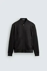 Cazadora bomber negra de corte regular fit, confeccionada en tejido efecto ante. Cuenta con cuello, puños y bajo en rib elástico, manga larga, bolsillos de vivo en la cadera y un bolsillo interior. Cierre frontal con cremallera.