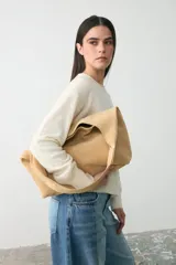 Cartera tipo tote de tamaño mediano, confeccionada en cuero suave de color beige. Presenta un diseño minimalista y amplio con bolsillo interior.