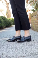 Zapato de cuero negro con puntera charolada, laterales texturados y pequeño taco cuadrado.