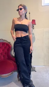 Pantalón negro de gamuza con flecos en los laterales, tiro alto y ajuste con cordones.