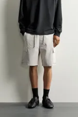 Bermuda cargo color negro de corte relaxed fit, confeccionada en tejido de algodón con elasticidad y efecto lavado. Cuenta con cintura elástica ajustable con cordón, bolsillos frontales y bolsillos laterales tipo cargo con solapa en las perneras.