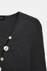 Chaqueta de punto color gris oscuro, con escote en pico y manga larga. Presenta cierre frontal con botones nacarados dispuestos de manera asimétrica.