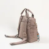 Mochila de diseño acolchado con pespuntes geométricos, color caqui. Cuenta con doble asa superior, bolsillo frontal con cierre y compartimentos laterales. Incluye un colgante decorativo con cuentas de colores en el cierre frontal.