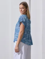 Blusa de lyocell color celeste con estampado de motivos playeros en blanco. Tiene cuello a la base con escote en V, mangas cortas con volados y detalle fruncido en mangas y espalda.