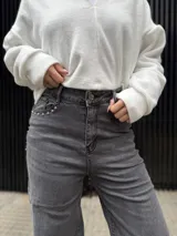 Pantalón de corte recto en color negro, confeccionado en tela elastizada de alta calidad. Presenta un diseño de tiro medio con detalle de tachas metálicas en la zona de los bolsillos delanteros.