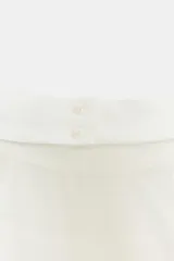 Top de cuello halter color blanco, con múltiples volantes en cascada en todo el frente y la espalda descubierta con cierre de botones y lazada en el cuello.