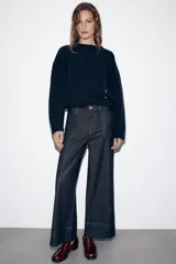 Pantalón de jean tiro medio con corte culotte, pernera ancha y corta. Presenta bolsillos delanteros de plastrón, costuras decorativas verticales y cierre frontal con cremallera y botón.